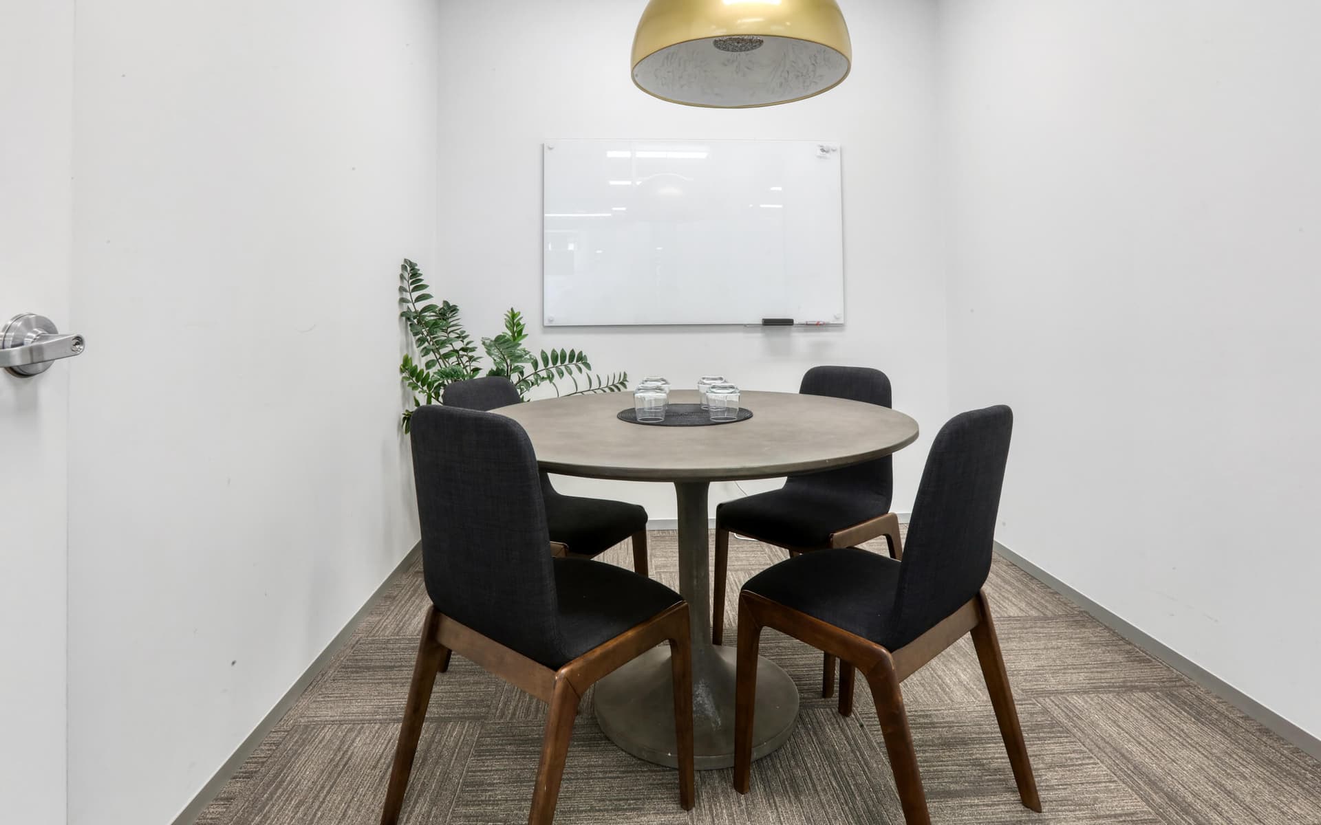 Small meeting room with round table, four chairs, and whiteboard. Modern, minimalist office space.