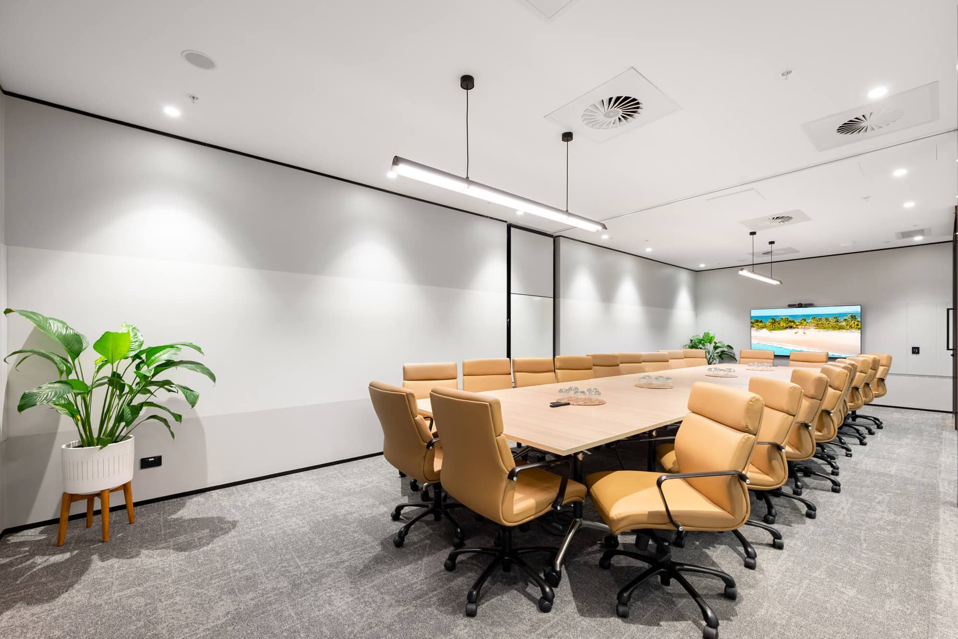 Bright modern conference room with a large table, tan leather chairs, and beach scene on a wall-mounted TV.