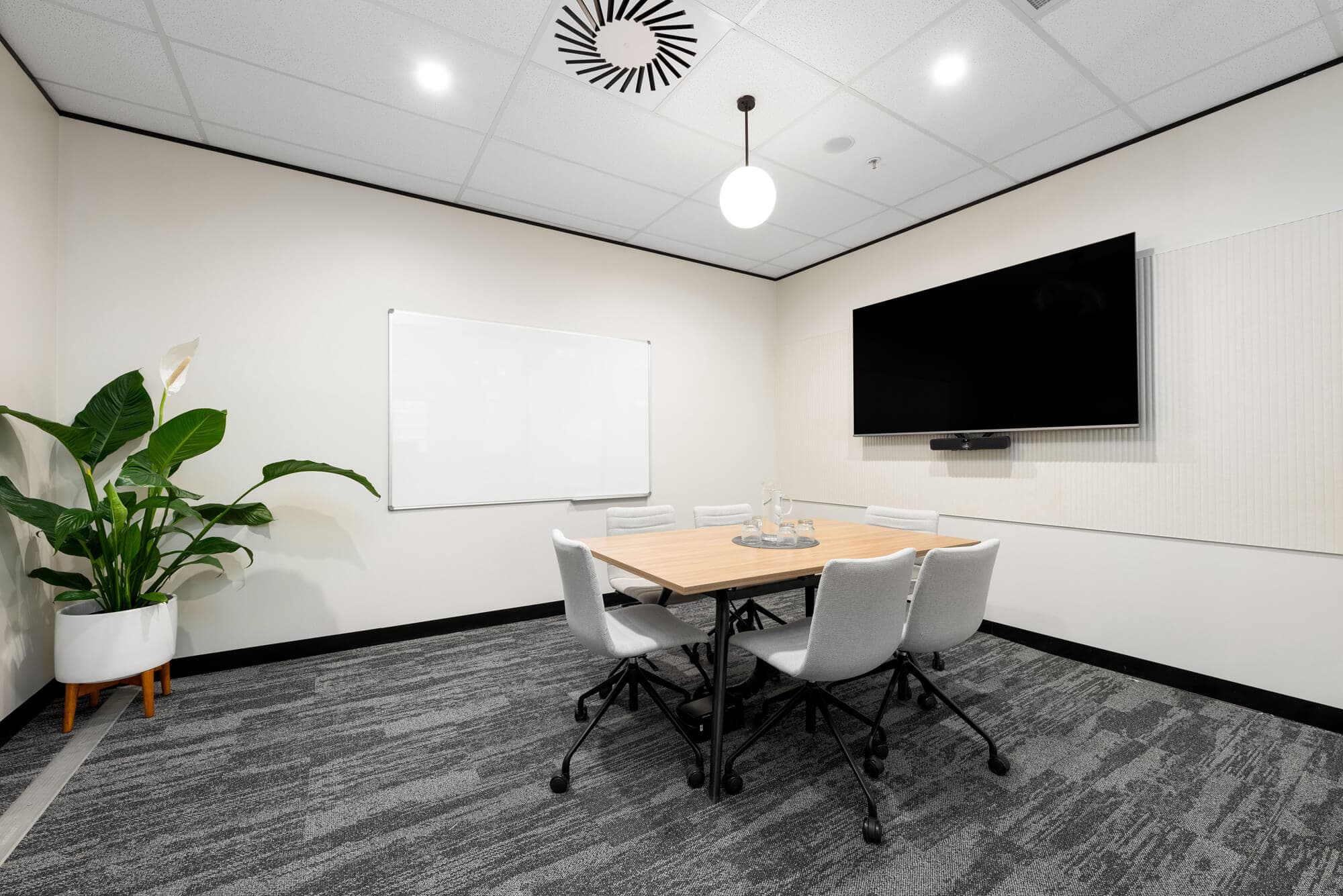 Small conference room with a dark wood table, grey chairs, whiteboard, and large screen on the wall.