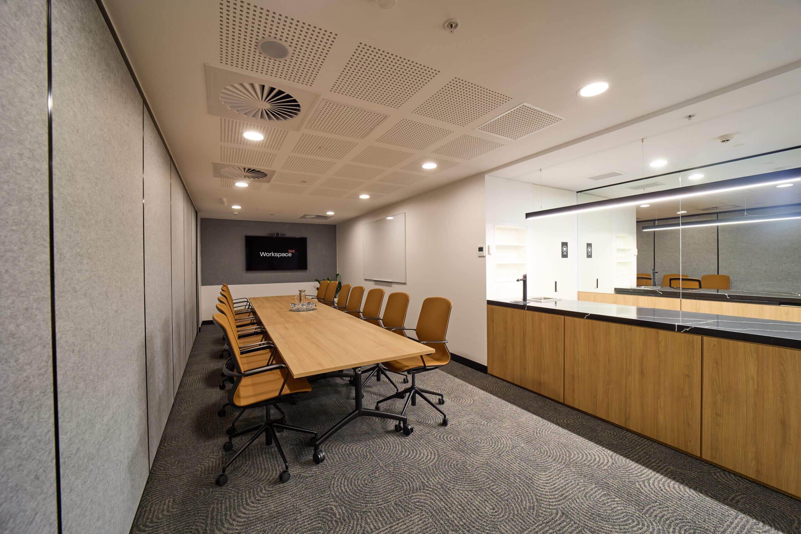Modern conference room with a long table, office chairs, a wall-mounted screen.