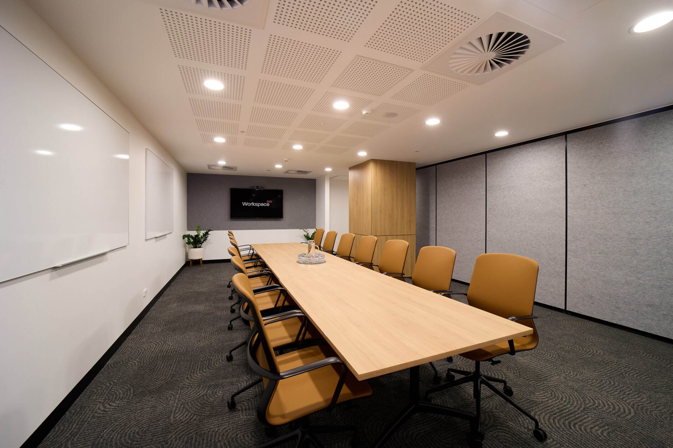 Conference room with a long table, multiple chairs, a monitor displaying "Workspace," and a ceiling with a drop tile pattern.